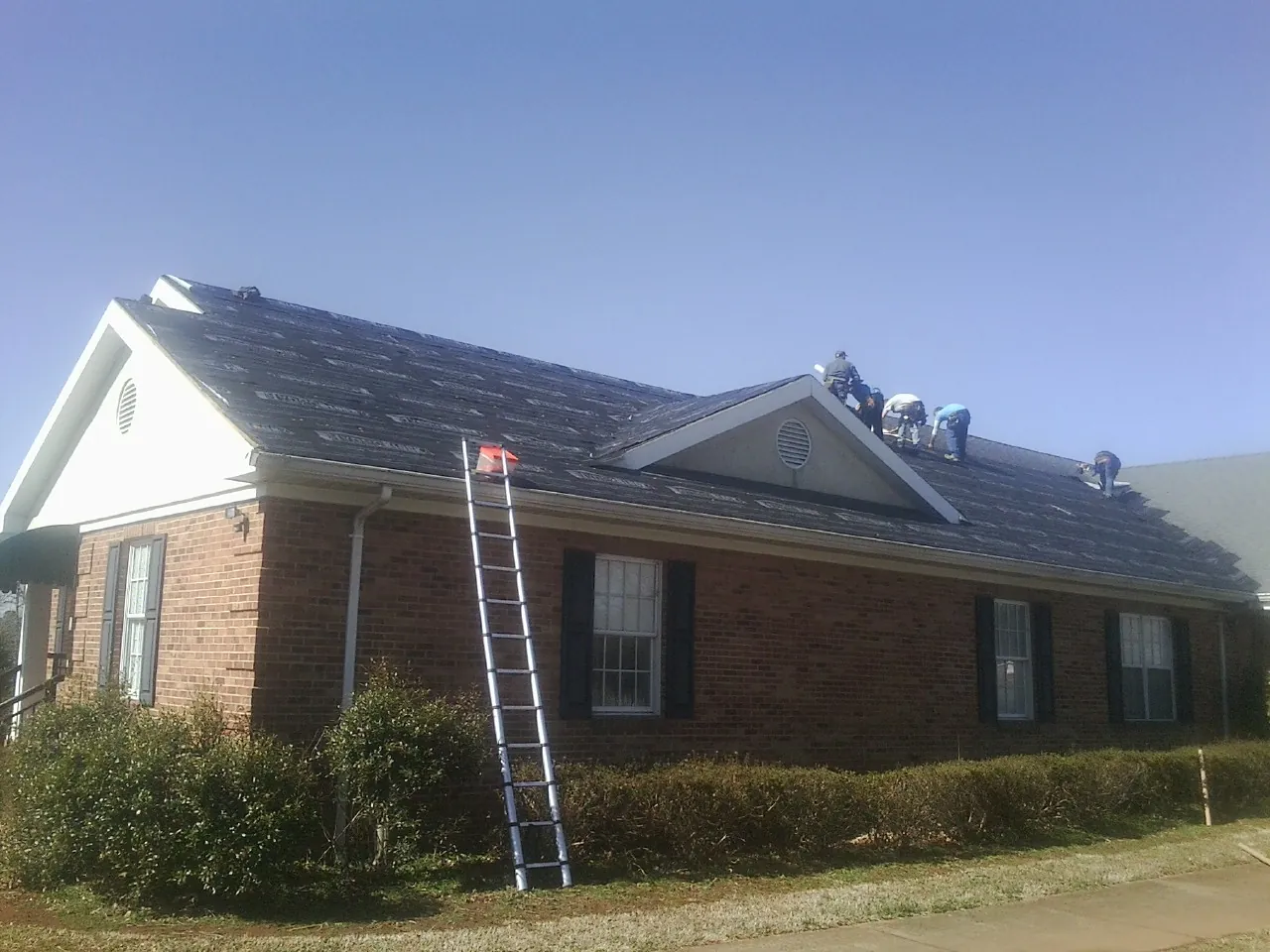 Crew tearing shingles off a brick ranch roof with a ladder set — Metal Roof Repair work by our crew in Waterville Valley