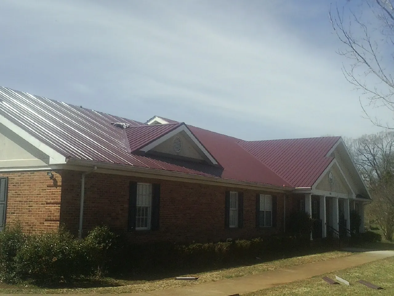 Red metal roof with gabled entries on a long brick building, from a Hail Damage Roof Repair job in Waterville Valley