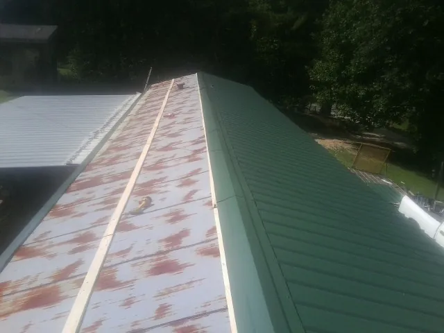 Old rusted panels beside newly installed green metal roofing — Wind Damage Roof Repair by Roofing Brothers in Waterville Valley