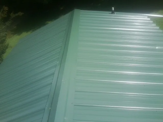 New green metal panels meeting at the ridge of a roof — Flat Roof Repair work by our crew in Waterville Valley