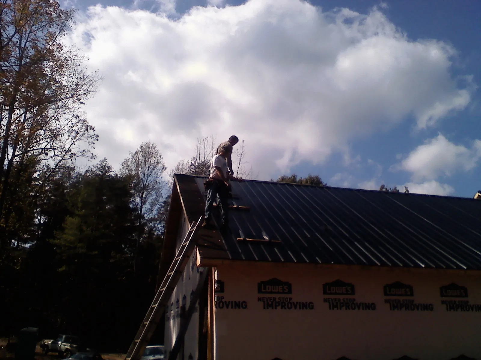 Roofer fastening dark metal panels high against a cloudy sky, from a Roof Inspection job in Waterville Valley