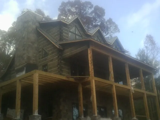 Stone chimney and dormers on a large log home with a timber porch in Waterville Valley