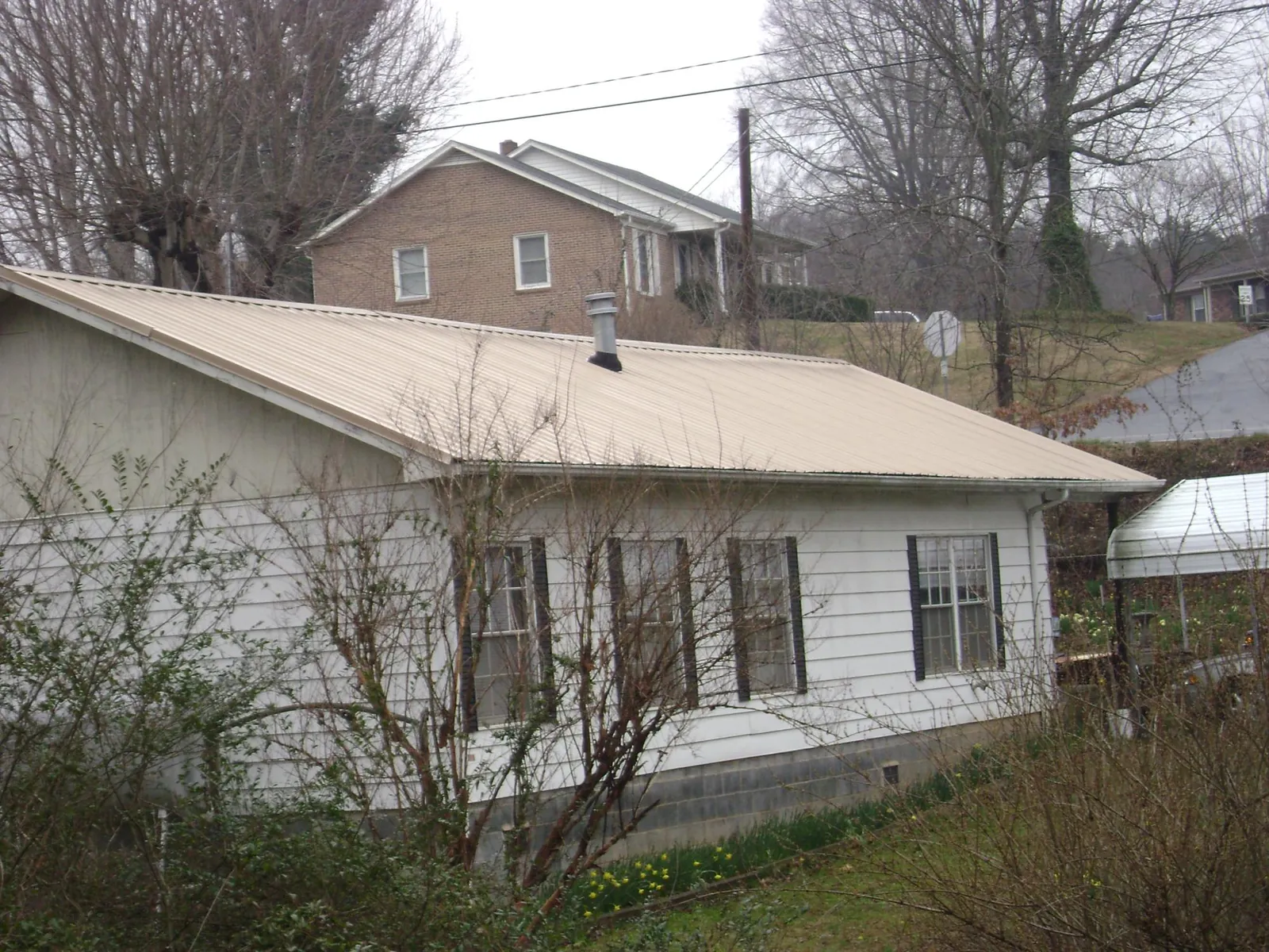 Tan metal roof on a white sided house set into a hillside — Commercial Roofing by Roofing Brothers in Waterville Valley