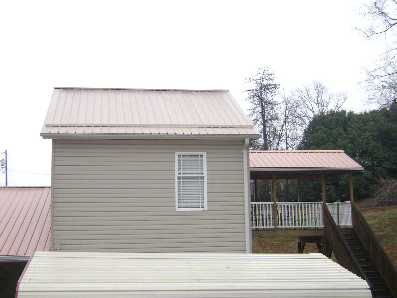 Tan metal roofs on a two story addition and attached porch, from a Roof Replacement job in Waterville Valley